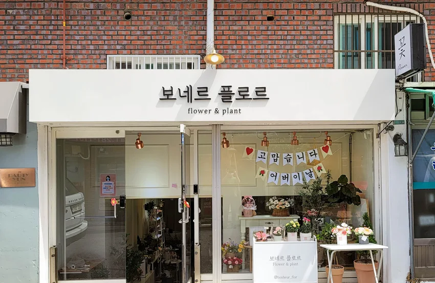 보네르 플로르 · 꽃과 함께 보이는 담백한 흰 간판 · 실제 시공 사진